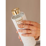 Wasserflasche mit goldenem Deckel glänzend und weiss gemusterter Schutzhülle.