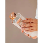 Wasserflasche mit bronzenem Deckel glänzend und weiss grau rosa pastell gemusterter Schutzhülle.