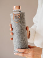 Stylishe Trinkflasche aus Glas mit hellgrauer melierter Filzhülle mit rose gold Tragegriff und rose gold Deckel.