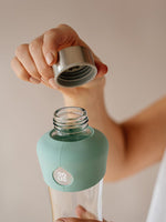 Stilvolle und zeitlose Glas Trinkflasche mit Silikonschutz unten und oben (Farbe mint oder zartes pastellgrün) für unterwegs. Trinkflasche Glas transparent ohne Design oder Druck ausser EQUA Logo in weiss.