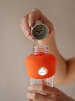 Stilvolle und zeitlose Glas Trinkflasche mit Silikonschutz unten und oben (Farbe tangerine oder leuchtendes mandarinenfarbenes orange) für unterwegs. Trinkflasche Glas transparent ohne Design oder Druck ausser EQUA Logo in weiss.