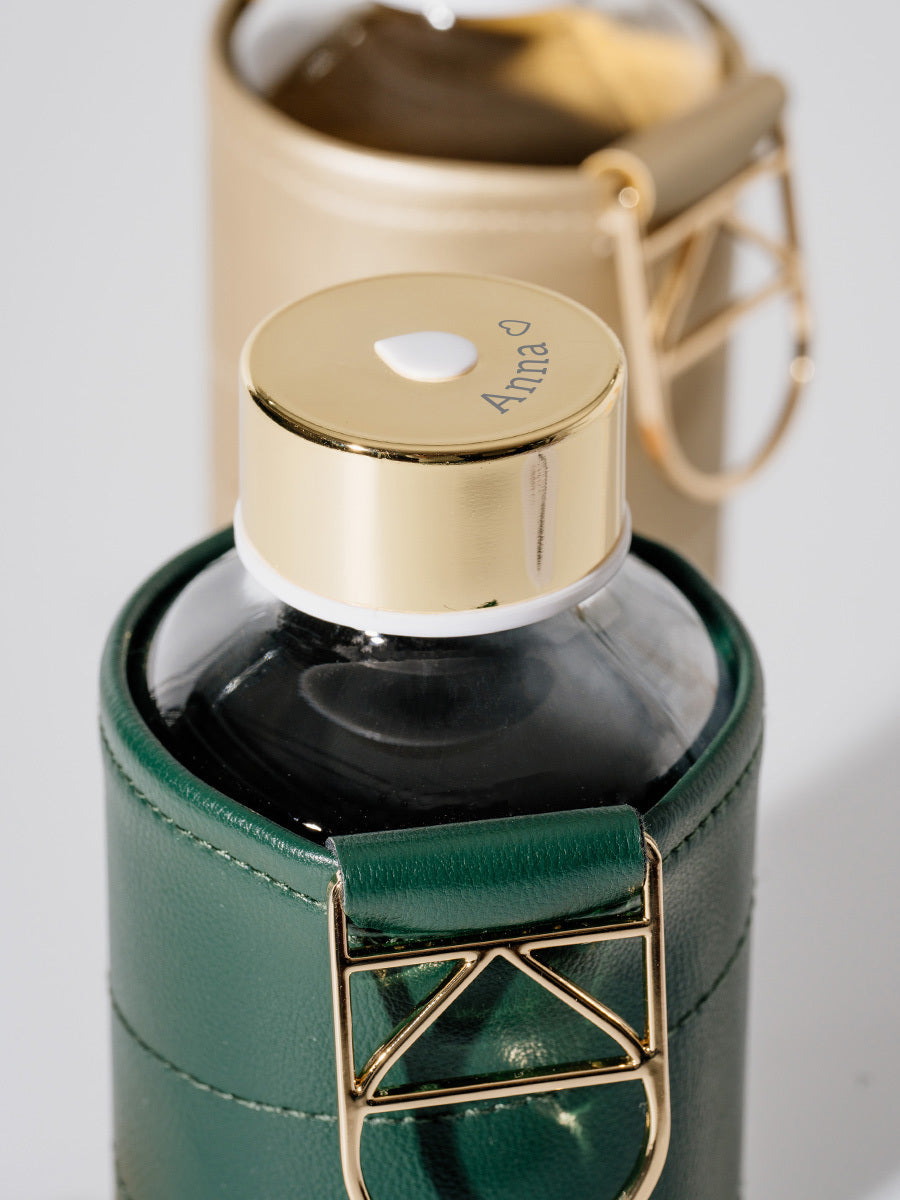 Glastrinkflasche kann ergänzt werden mit zahlreichen passenden Schutzhüllen aus faux-leather oder Filz. Schützt die Glasflasche auch für den Gebrauch unterwegs. Diese Glaswasserflasche kommt in einer dunkelgrünen Hülle - chic und gut kombinierbar. Deckel in gold kann wie auf dem Bild mit eigenem Text graviert werden.